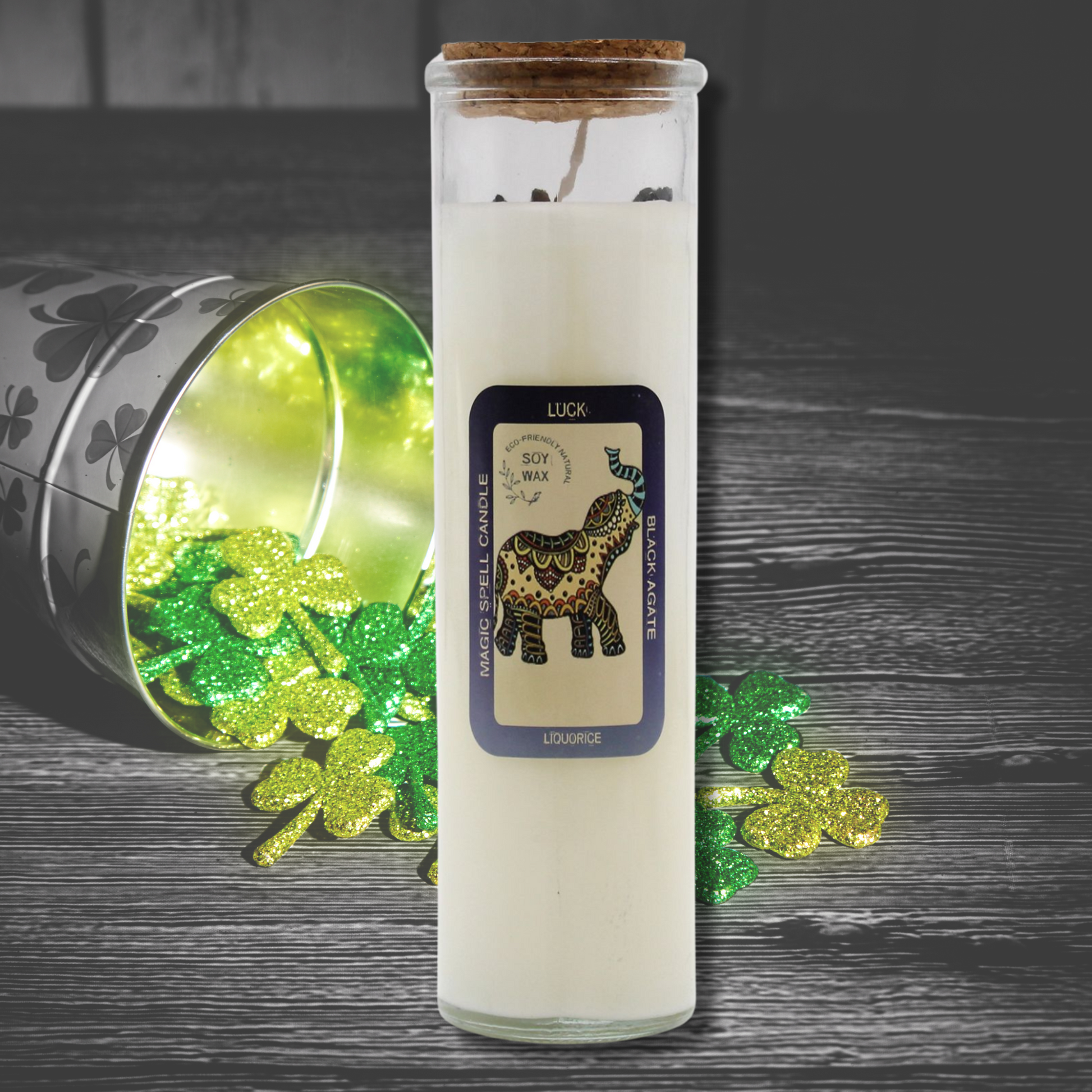 Candle in a glass jar with a label featuring a horse design, surrounded by green shamrock leaves on a dark surface.